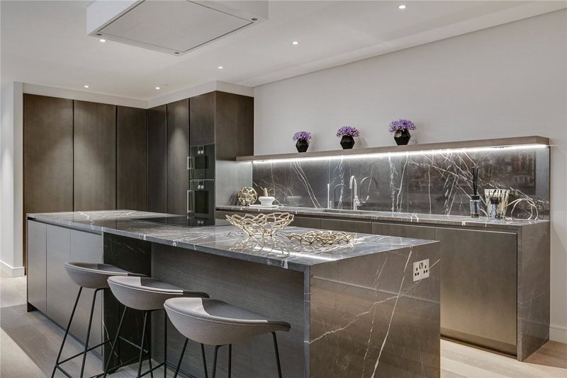 Kitchen with a dark marble island, bronze units and integrated ovens.