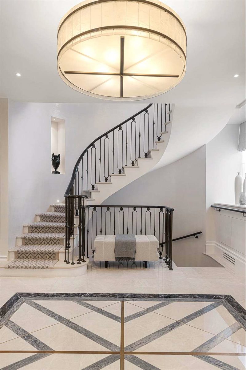 A stair hall in a finished Knightsbridge townhouse: a curved stone stair with iron balusters and an inlaid marble floor.